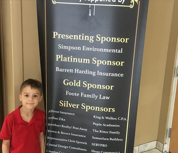 Young boy in red shirt standing in front of black banner listing sponsors